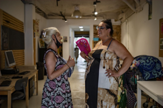 Photo of two women talking to each other, one of them is holding a handheld fan.