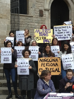 Photo shows shows four people with posters at a protest and in the middle a woman with a megaphone speaking.